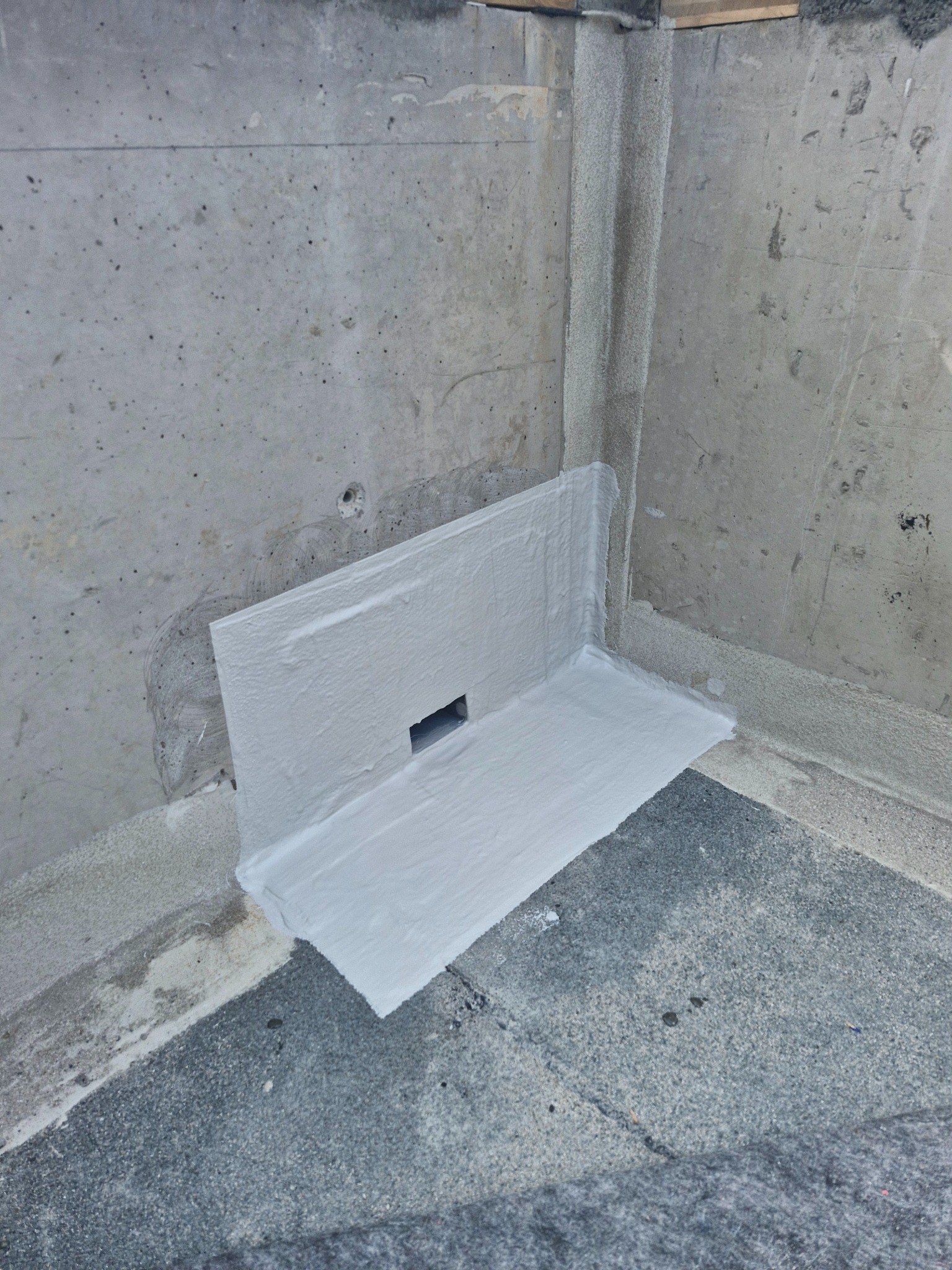 Szczegółowe uszczelnienie narożnika dachu z odpływem, zabezpieczone białą, elastyczną powłoką hydroizolacyjną na szarej powierzchni dachu i betonowych ścianach.