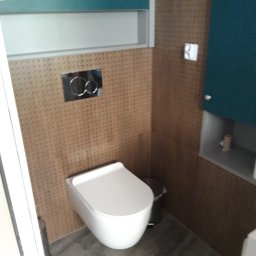 Andrzej Wierczyński - Nowoczesna toaleta podwieszana z zabudową w brązowej mozaice i turkusowymi szafkami. Minimalistyczny design, szara podłoga, chromowane detale.