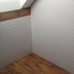 Andrzej Wierczyński - Wykończona łazienka na poddaszu: białe płytki z delikatnym wzorem na ścianach, drewnopodobna podłoga i listwa dekoracyjna. Widoczne otwory na gniazdka.