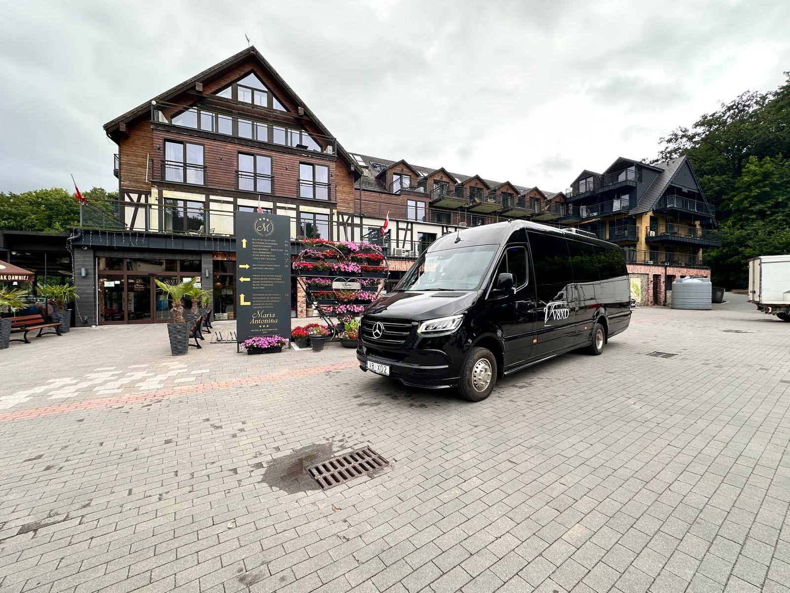 Czarny, luksusowy bus Mercedes-Benz Sprinter z przyciemnianymi szybami, zaparkowany przed hotelem Maria Antonina. Elegancki transport dla wymagających klientów.