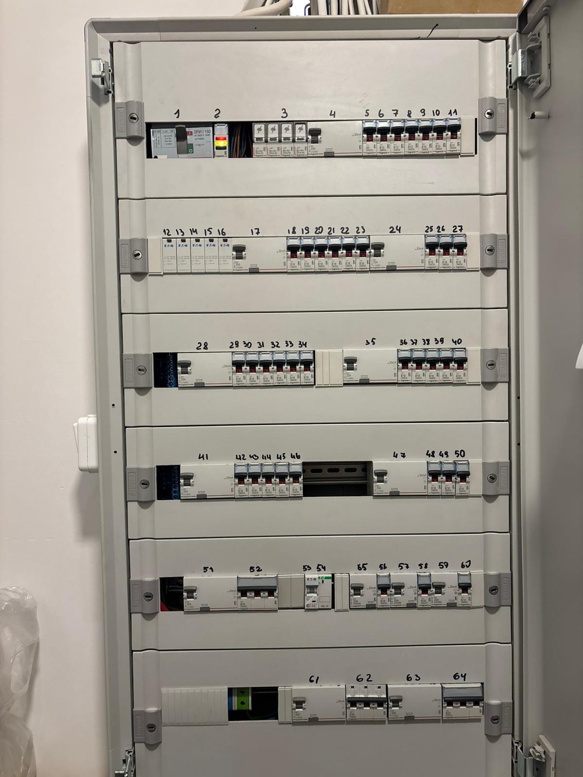 Rozdzielnica elektryczna z numerowanymi bezpiecznikami, widok z bliska. Bezpieczniki różnych typów i marek. Otwarta obudowa rozdzielnicy.