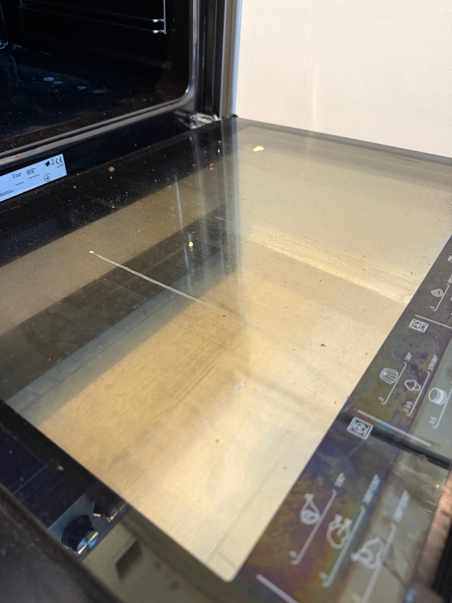 Brudna szyba piekarnika z widocznymi zabrudzeniami i resztkami jedzenia, wymagająca dokładnego czyszczenia. Widoczne oznaczenia na panelu sterowania.