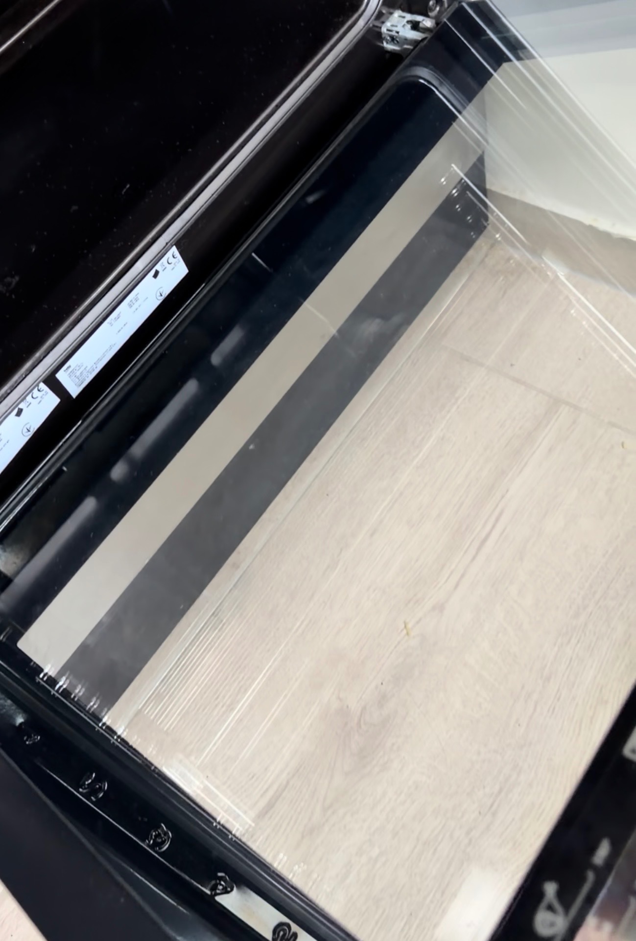 Wnętrze czystego piekarnika z otwartymi drzwiczkami, ukazujące jasne, drewnopodobne dno. Widoczne detale konstrukcyjne i uszczelki.