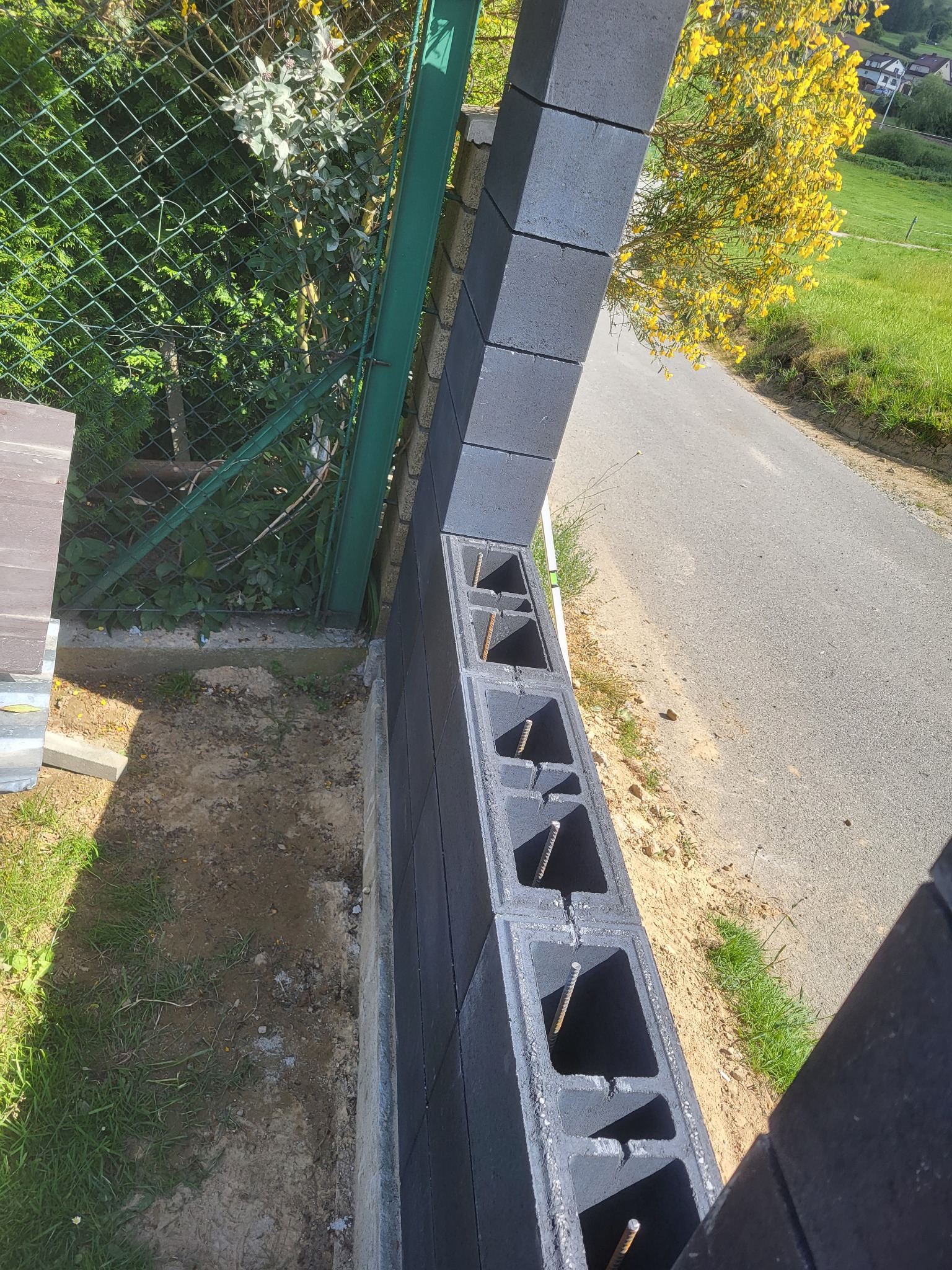 Budowa ogrodzenia z bloczków betonowych w Czarnym Dunajcu. Widoczne zbrojenie wewnątrz pustaków. Etap wznoszenia muru, zielone otoczenie.