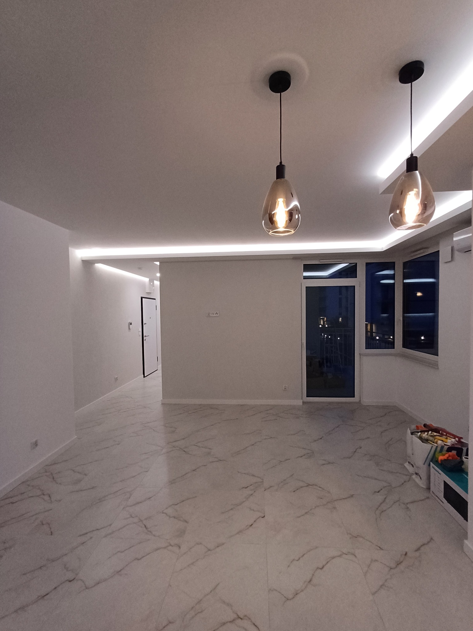 Wykończone wnętrze mieszkania z marmurową podłogą, nowoczesnym oświetleniem LED i wiszącymi lampami. Widok na okno balkonowe i drzwi wejściowe.