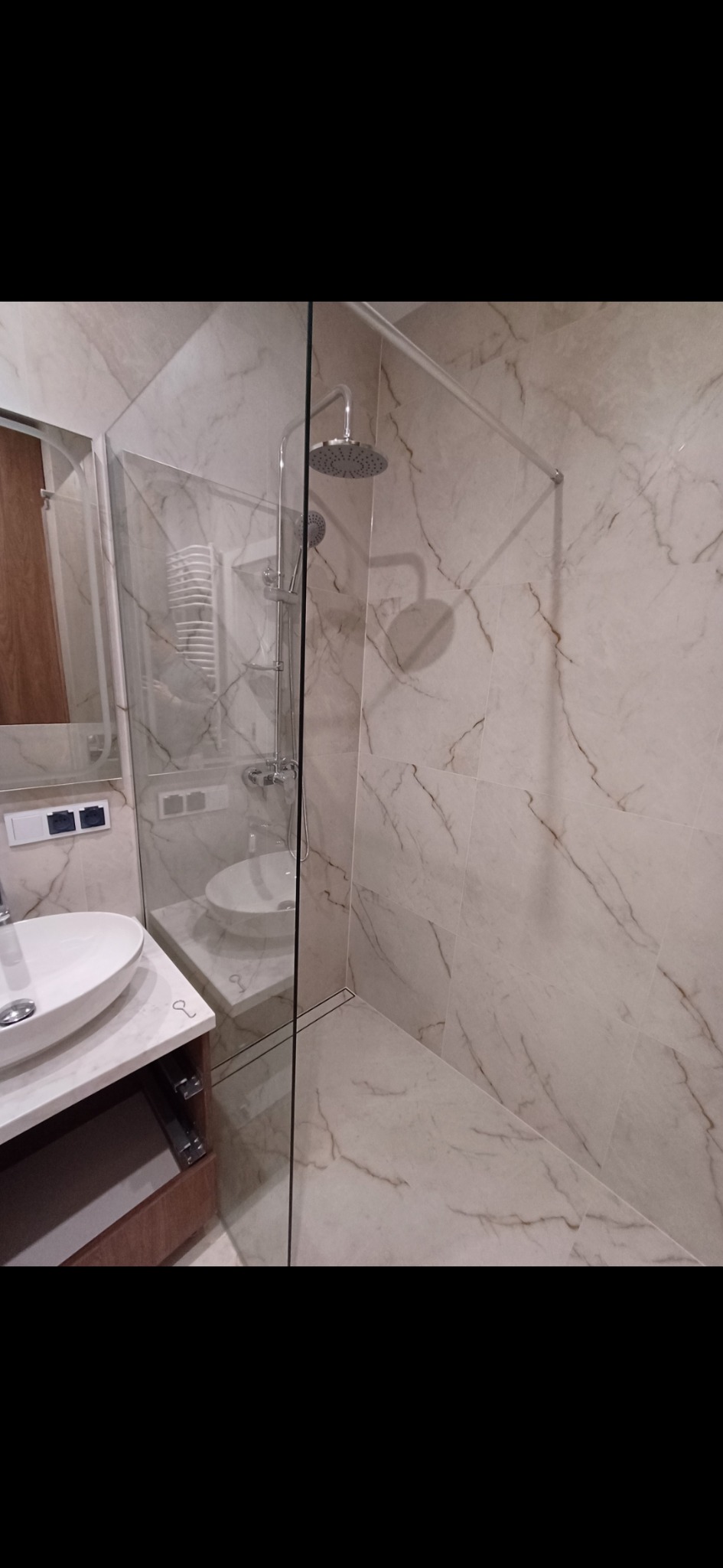 Wykończona łazienka z kabiną prysznicową typu walk-in, umywalką nablatową i marmurowymi płytkami w odcieniach beżu z brązowymi żyłami.