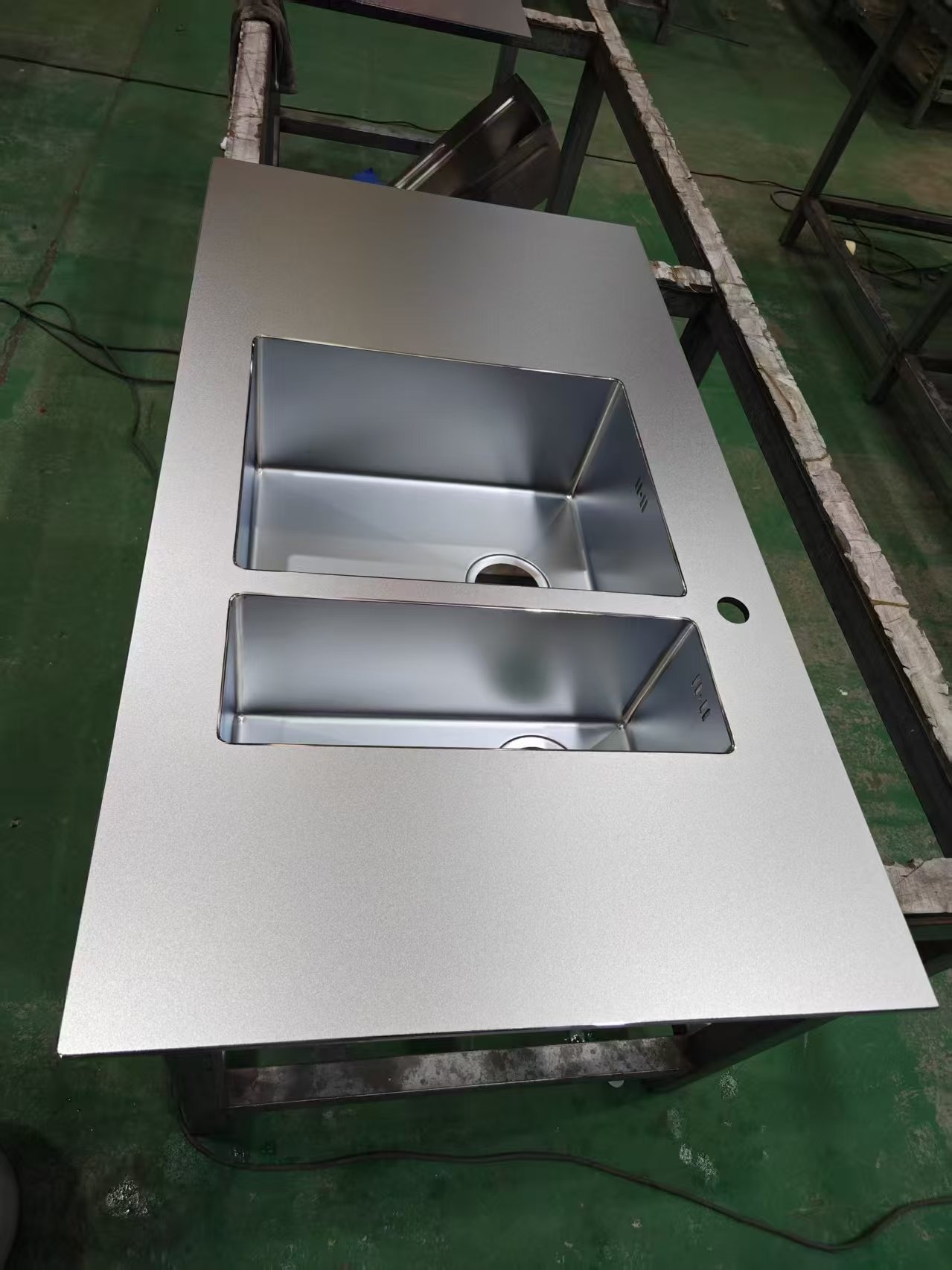 Stalowy blat kuchenny z dwoma wbudowanymi zlewozmywakami, widoczne detale wykończenia i otwór na baterię. Surowy, industrialny styl. Ujęcie z góry.