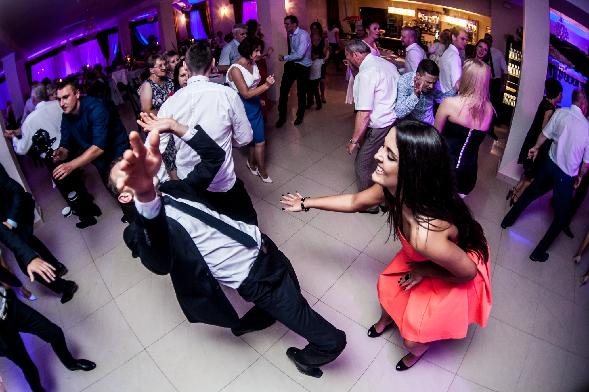 Roztańczona para na parkiecie podczas wesela, uchwycona z szerokiego kąta. W tle bawiący się goście i bar. Dynamiczne ujęcie z imprezy.