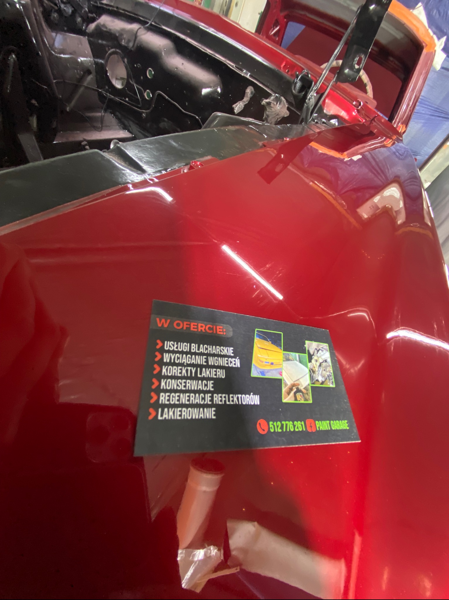 Czerwony, błyszczący element karoserii auta w Jaśliskach, po lakierowaniu. Widoczna naklejka z ofertą usług blacharskich i lakierniczych. Detal z bliska.