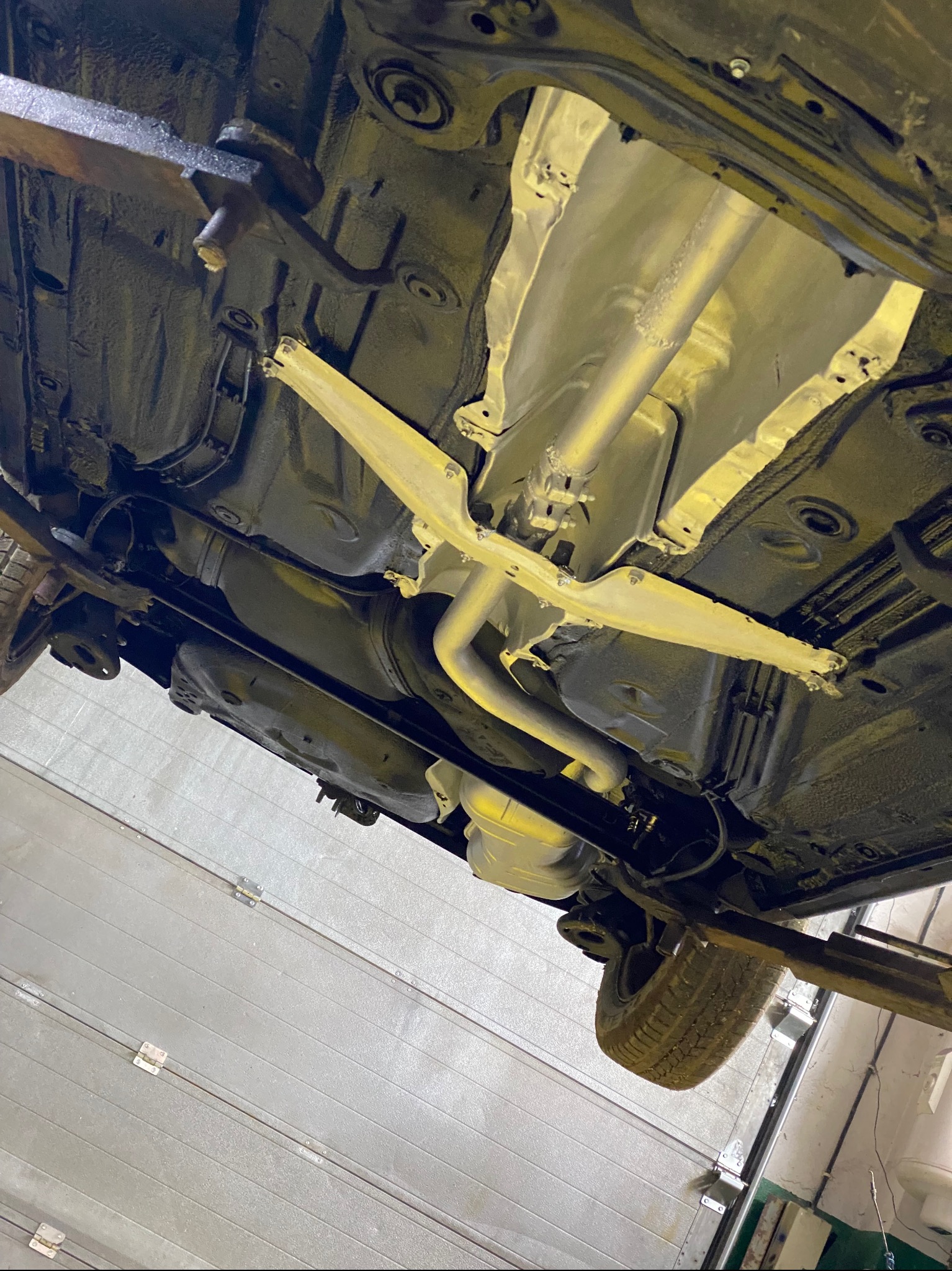 Podwozie auta po zabezpieczeniu antykorozyjnym, widoczne elementy zawieszenia i układu wydechowego. Auto na podnośniku w warsztacie.