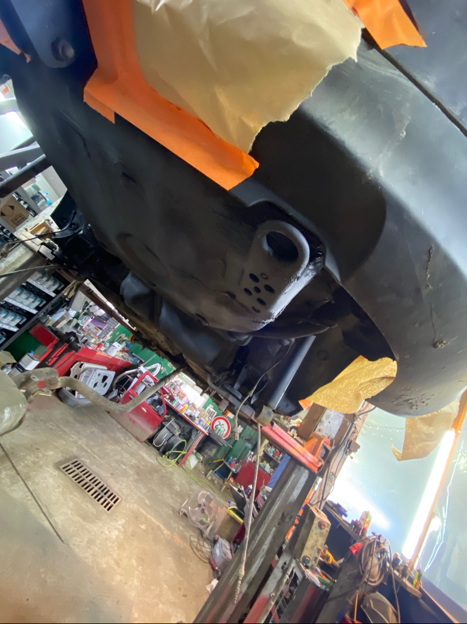 Podwozie auta po konserwacji antykorozyjnej, widoczne zabezpieczone elementy i taśma maskująca. Ujęcie z dołu, w warsztacie samochodowym.