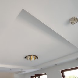 Jakub - Biały sufit podwieszany z dekoracyjnym wgłębieniem i punktowymi lampami w stylu glamour. Widoczne okno i fragment ściany. Minimalistyczny design z nutą elegancji.