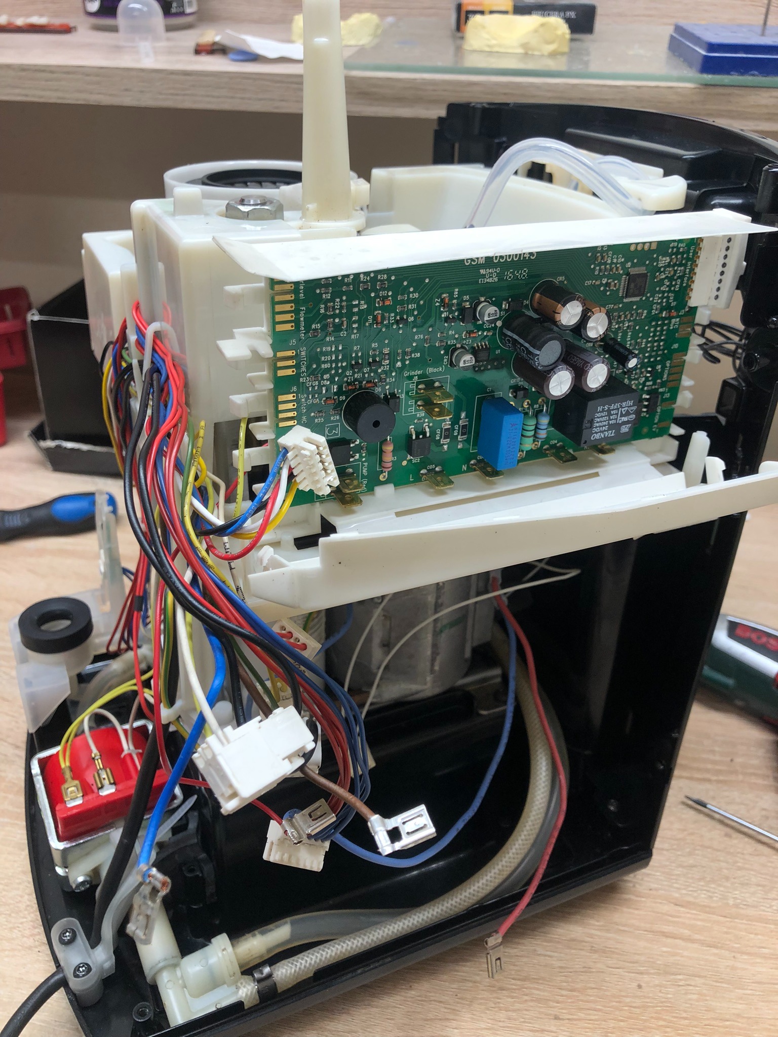 Rozłożony ekspres do kawy Krups z widoczną elektroniką i przewodami. Detaliczny widok wnętrza urządzenia podczas naprawy. Widoczne narzędzie.