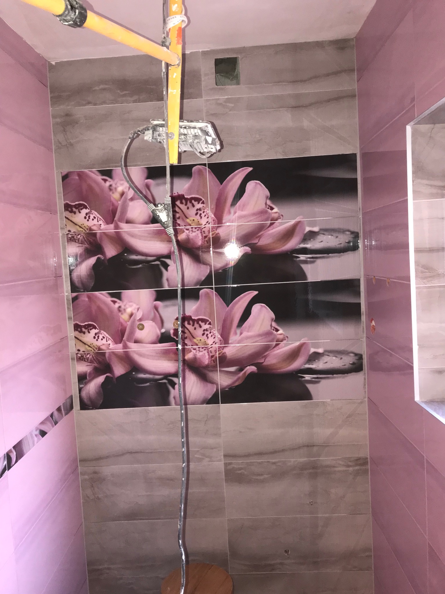 Różowe i szare płytki z motywem kwiatowym w łazience, widoczna instalacja prysznicowa w trakcie montażu.