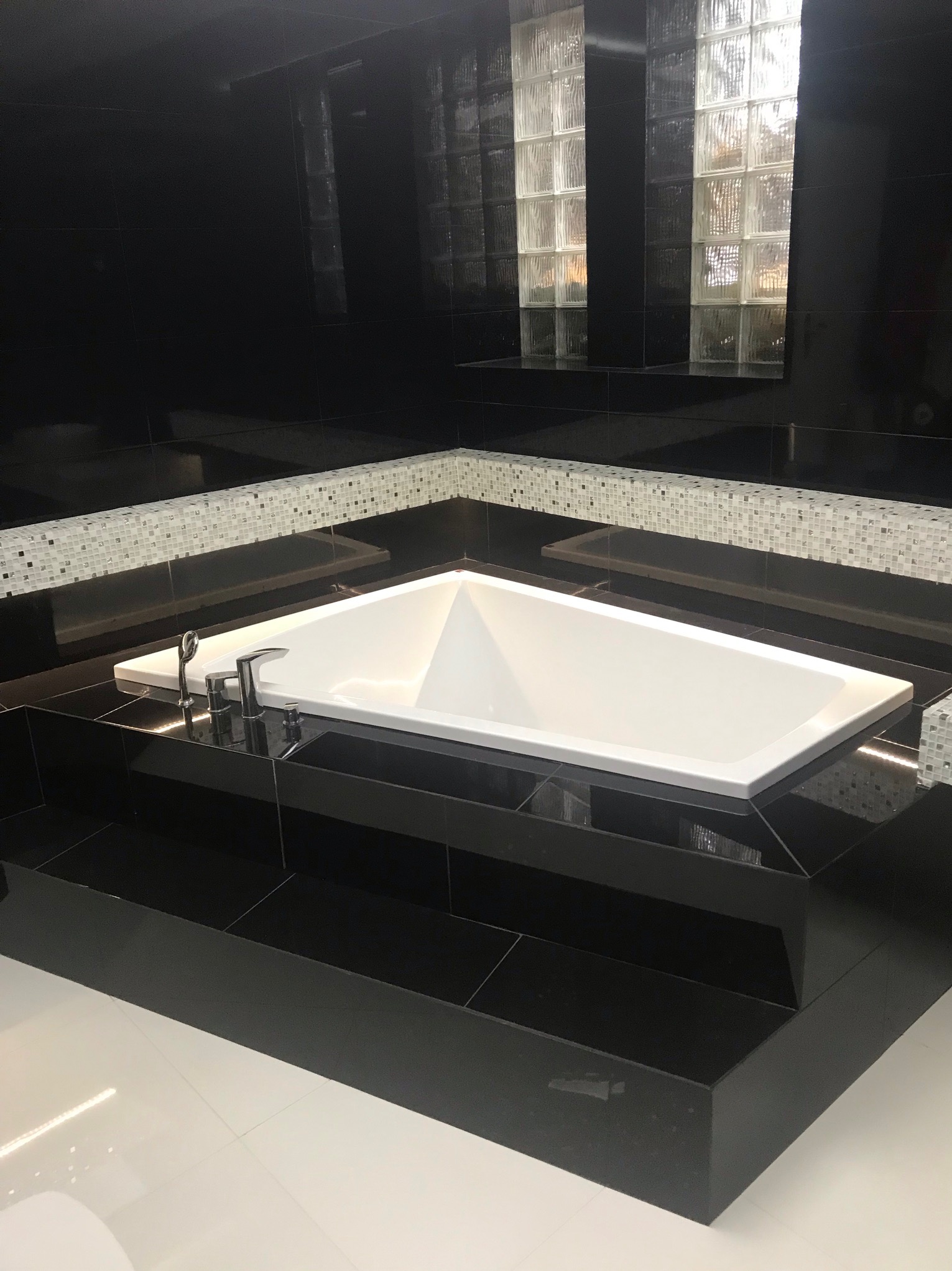 Nowoczesna łazienka w czerni i bieli z wanną w zabudowie, mozaiką i luksferami. Minimalistyczny design, eleganckie wykończenie, wysoki połysk płytek.