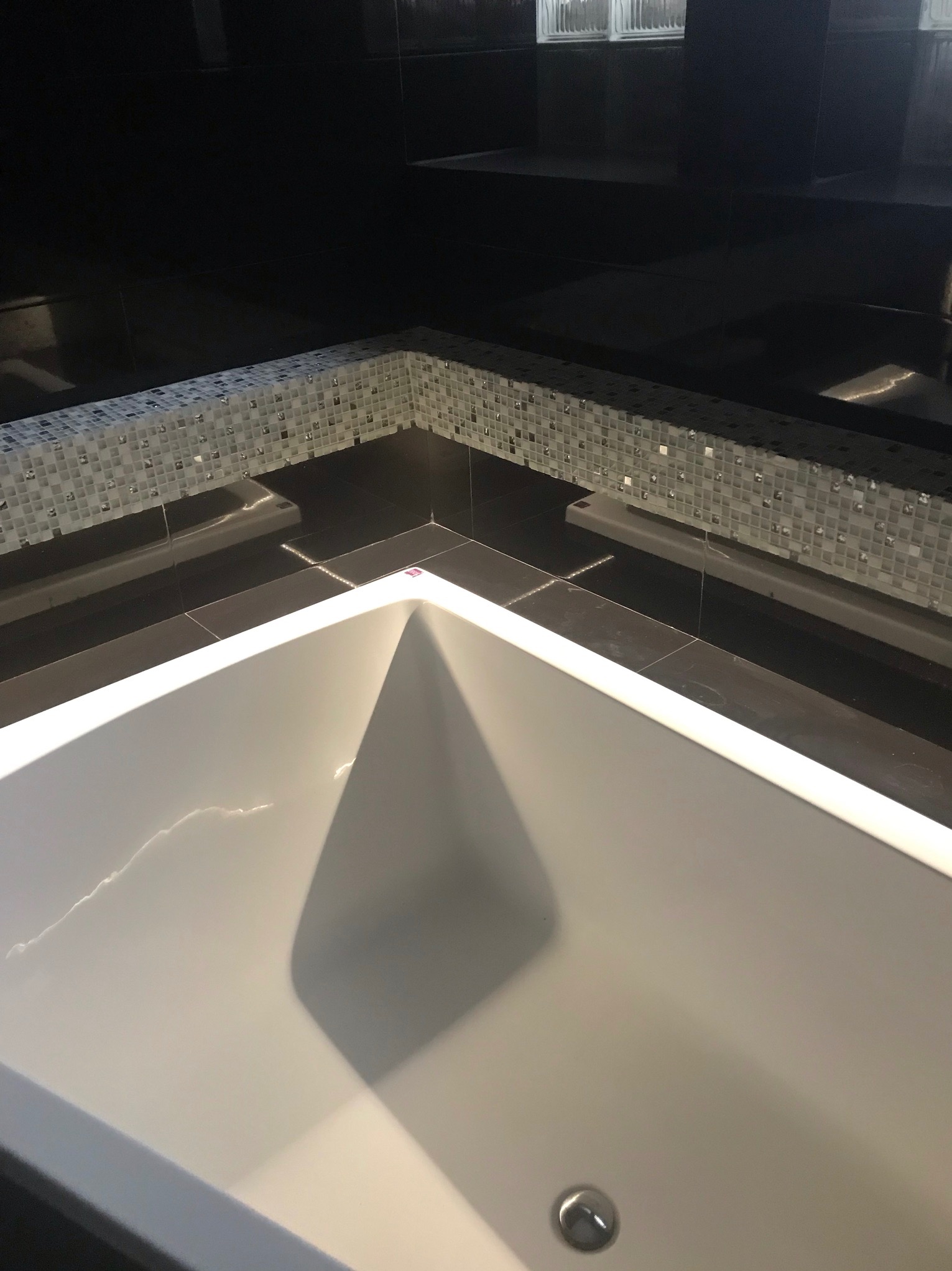 Biała wanna z oświetleniem LED, obłożona czarnymi płytkami i mozaiką w łazience. Widok z góry, nowoczesny design.