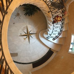 Grzegorz Sasinowski - Spiralne schody z kutą balustradą i marmurową posadzką z motywem kompasu, widok z góry. Dekoracja świąteczna na schodach.