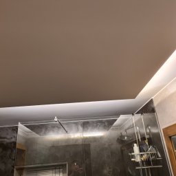 Grzegorz Sasinowski - Nowoczesna łazienka z kabiną prysznicową typu walk-in, wykończona płytkami imitującymi marmur i podświetlanym sufitem. Widoczne detale armatury i akcesoriów.