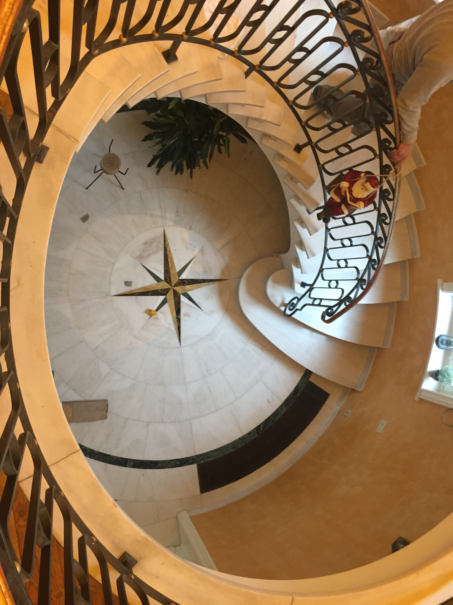 Spiralne schody z kutą balustradą i marmurową posadzką z motywem kompasu, widok z góry. Dekoracja świąteczna na schodach.