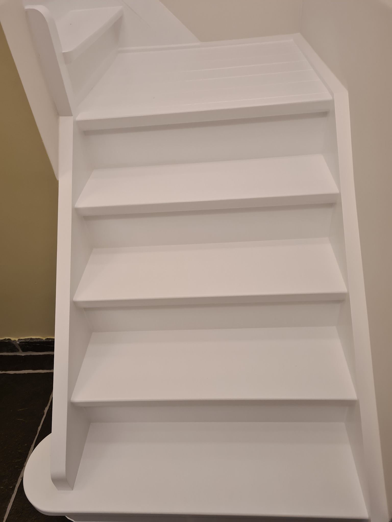 Białe, odnowione schody drewniane w domu, widok z dołu. Świeżo pomalowane stopnie i boki schodów, kontrastujące z ciemną podłogą i jasnymi ścianami.