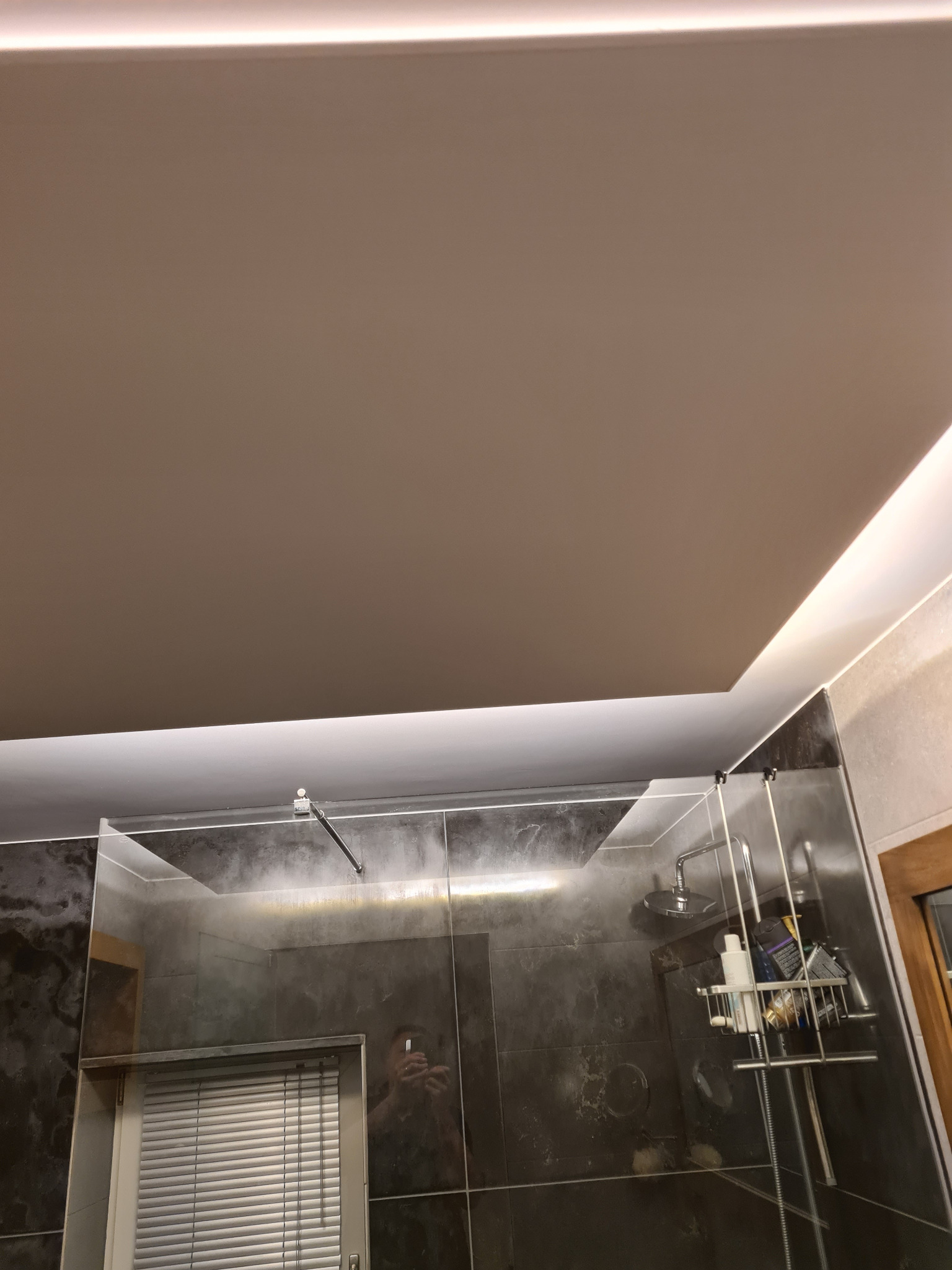 Nowoczesna łazienka z kabiną prysznicową typu walk-in, wykończona płytkami imitującymi marmur i podświetlanym sufitem. Widoczne detale armatury i akcesoriów.