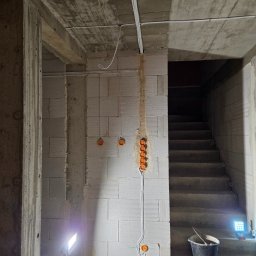 El-Home Piotr Janucik - Surowy stan: instalacja elektryczna w trakcie montażu w Księżynie. Widoczne kable i puszki na ścianie z betonu komórkowego, oświetlone lampą budowlaną.