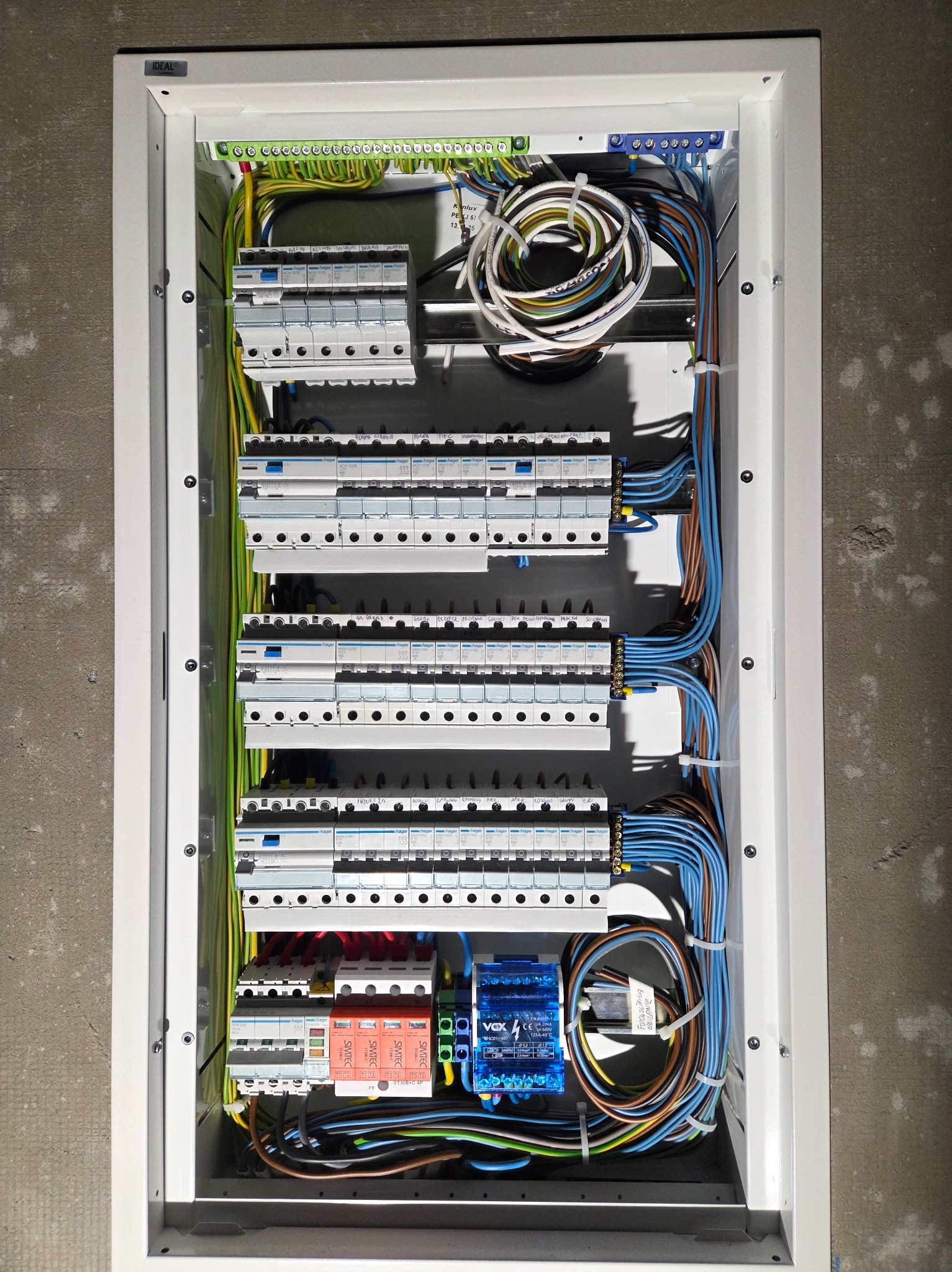 Rozdzielnica elektryczna w białej obudowie, z widocznymi bezpiecznikami, przewodami i elementami sterującymi. Instalacja schludna, z dbałością o detale.