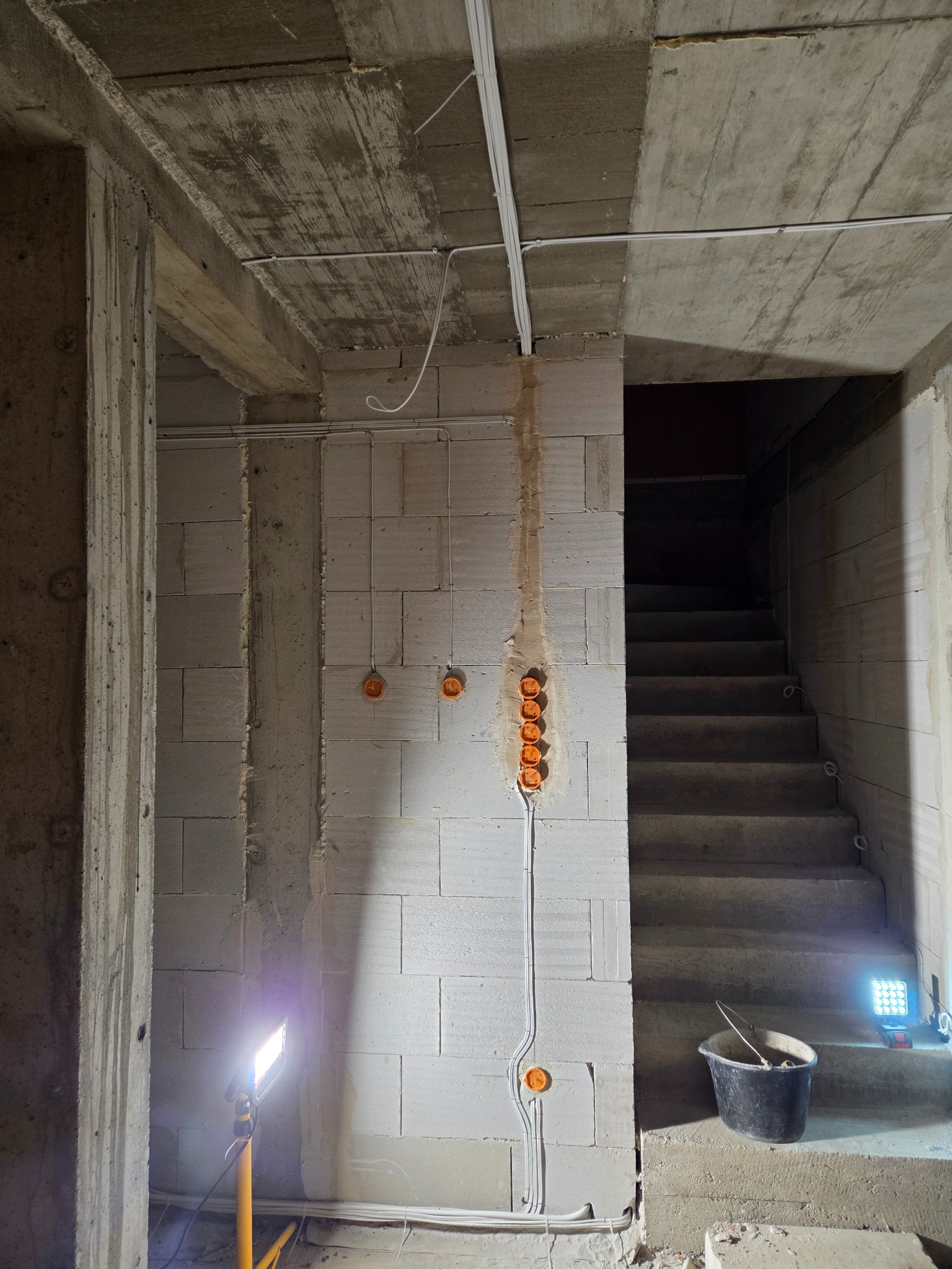 Surowy stan: instalacja elektryczna w trakcie montażu w Księżynie. Widoczne kable i puszki na ścianie z betonu komórkowego, oświetlone lampą budowlaną.