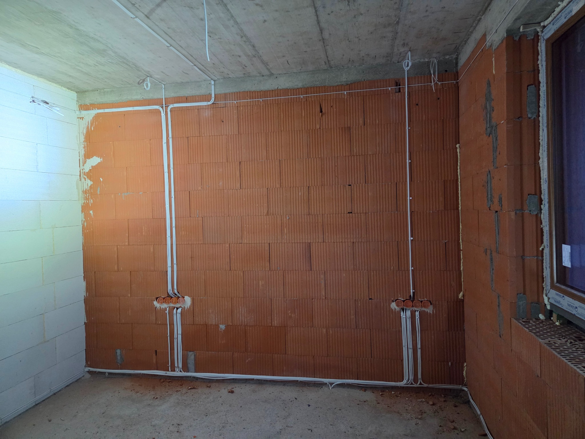 Surowy stan: Instalacja elektryczna w budynku z czerwonej cegły, widoczne kable w peszlach i puszki podtynkowe. Ściany nieotynkowane, surowy betonowy strop.