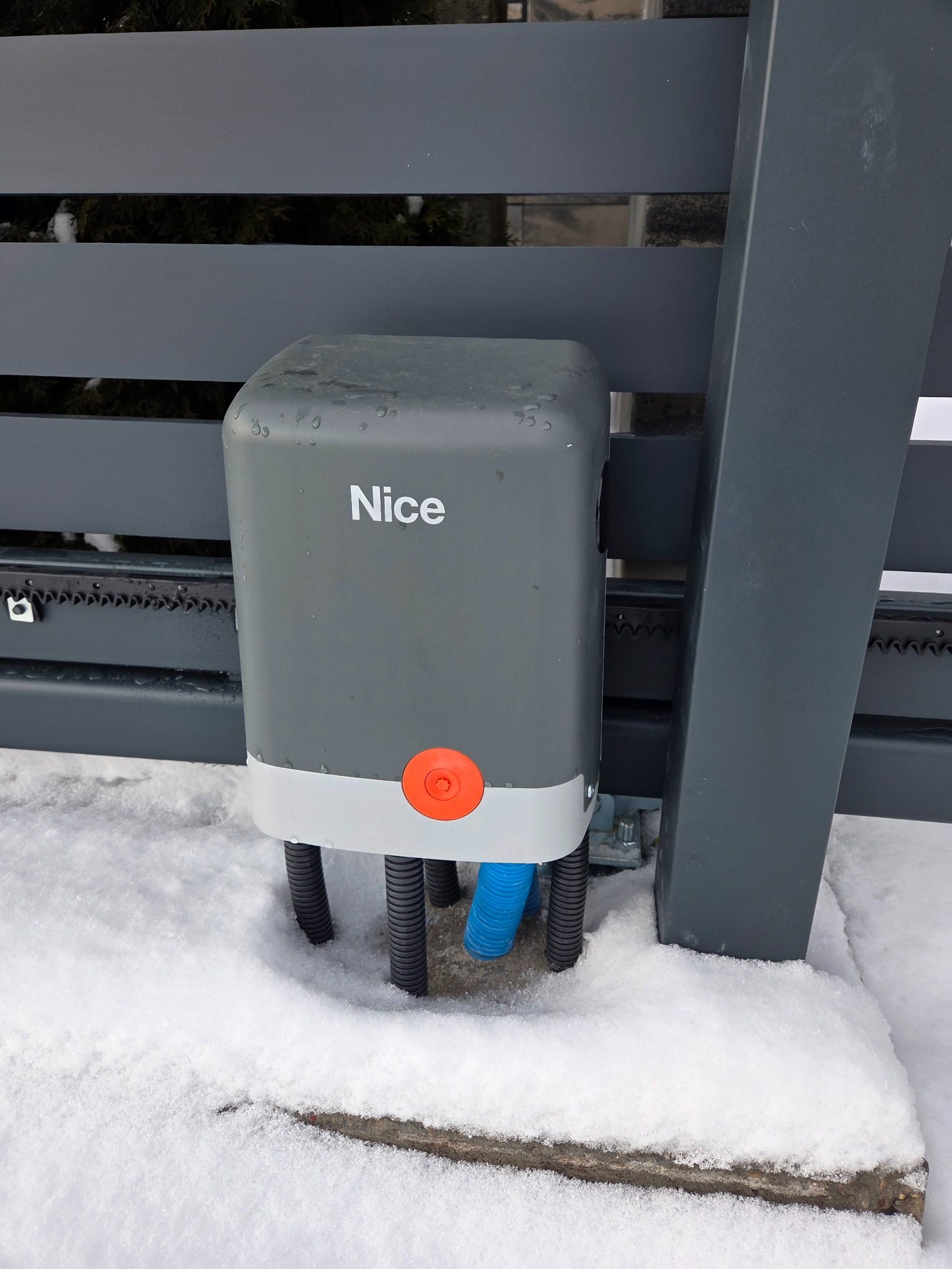 Szary napęd bramy Nice, zamontowany na metalowej konstrukcji w Księżynie, otoczony śniegiem. Widoczna listwa zębata i przewody. Detal z bliska.