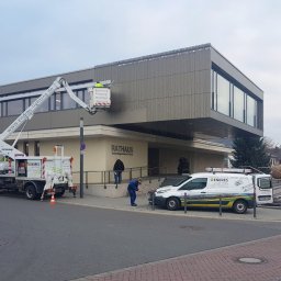 D-instal.NET Bartosz - Montaż oświetlenia zewnętrznego na budynku Ratusza z użyciem podnośnika koszowego firmy Endres Lighting. Pracownik w koszu, drugi na ziemi. Widoczny firmowy van.