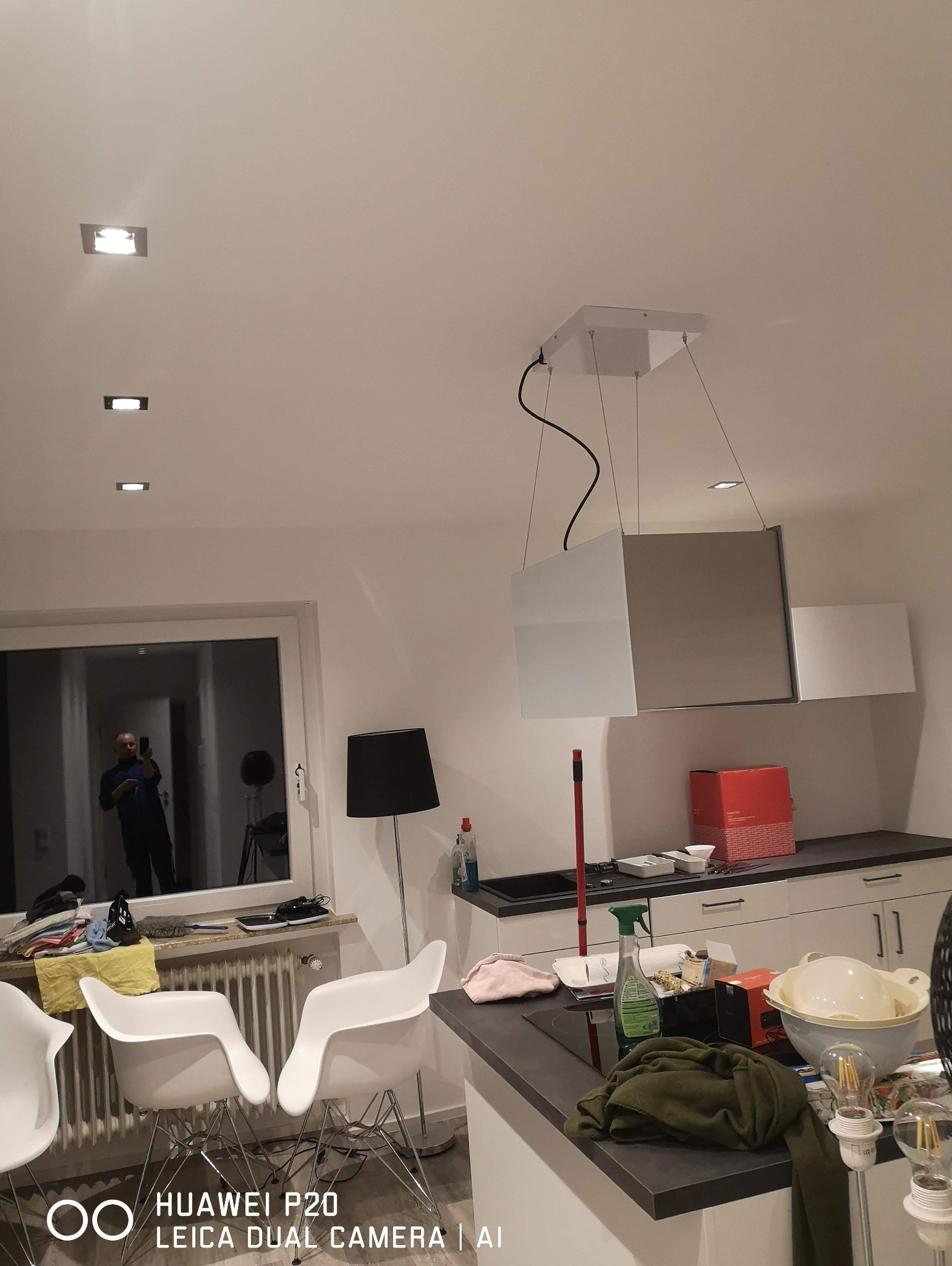 Nowoczesna kuchnia z zamontowanym oświetleniem sufitowym i reflektorami. W oknie odbija się osoba robiąca zdjęcie.