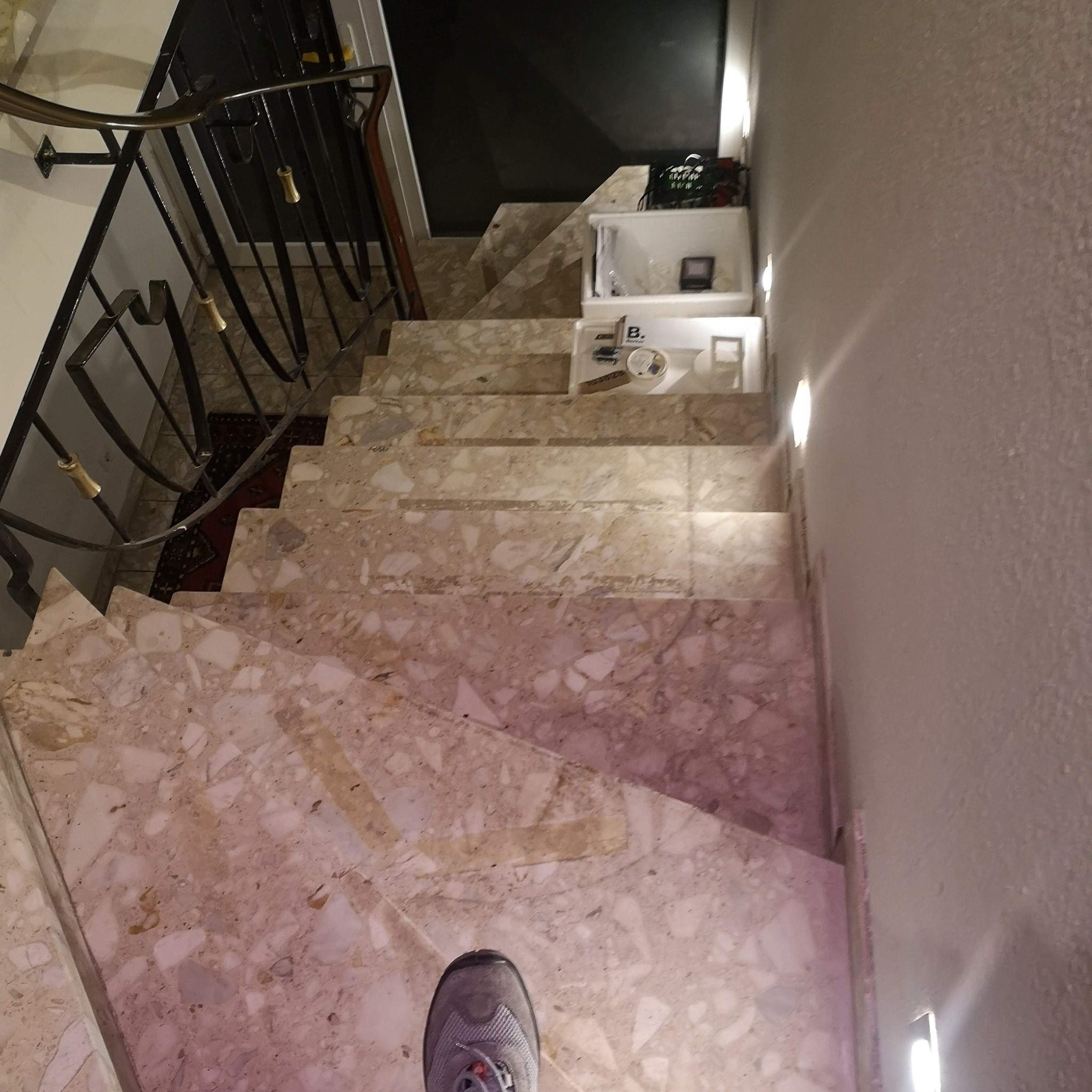 Marmurowe schody z zamontowanym oświetleniem LED w ścianie. Na schodach leżą opakowania po produktach elektrycznych. Widok z góry, stopa w kadrze.