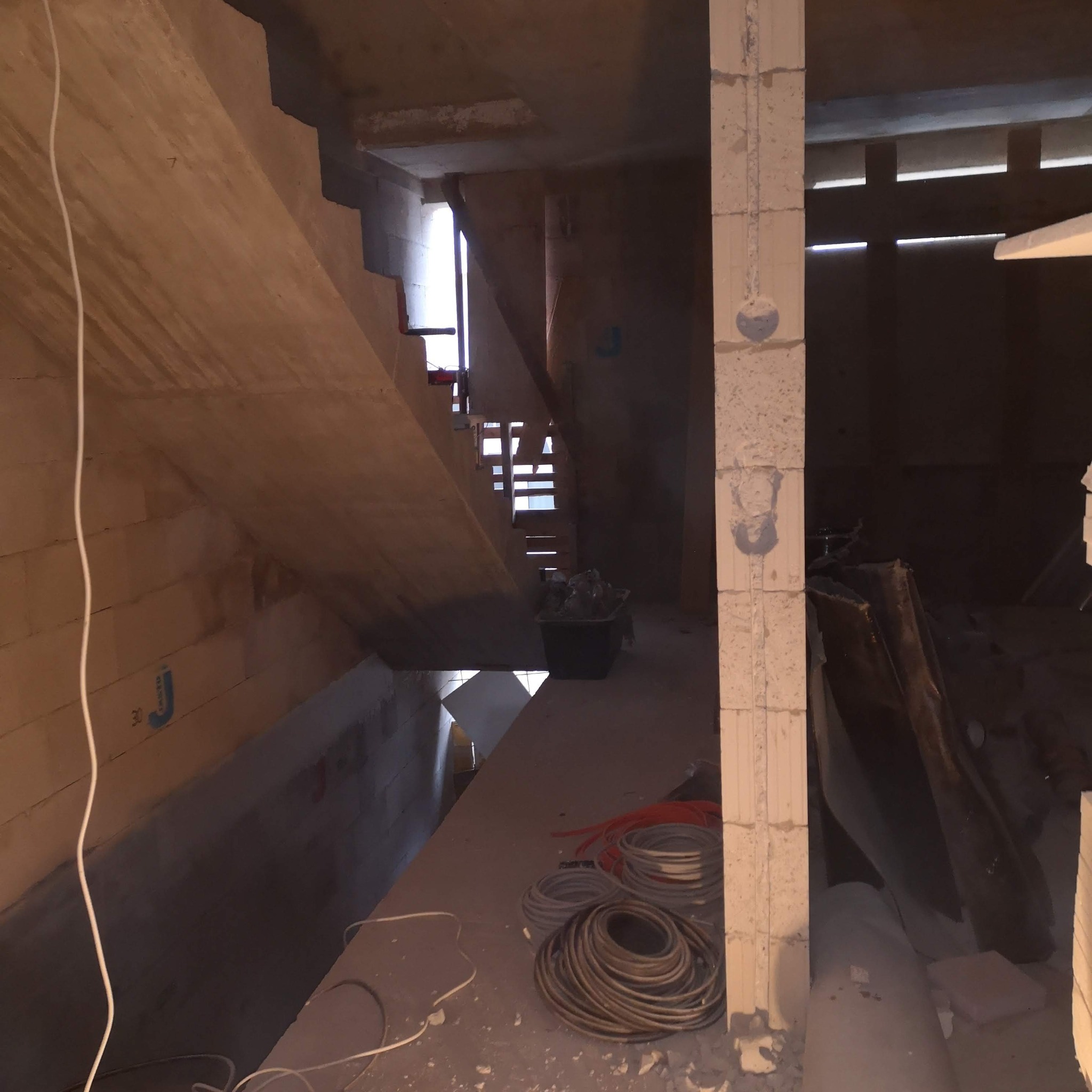 Surowy stan poddasza z widocznymi kablami elektrycznymi, przygotowanego do instalacji. Widoczne schody i ściany z betonu komórkowego.