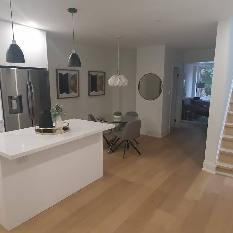 Nowoczesna kuchnia z wyspą i trzema lampami wiszącymi o różnych kształtach. Minimalistyczny design, jasne kolory, drewniana podłoga i okrągłe lustro.