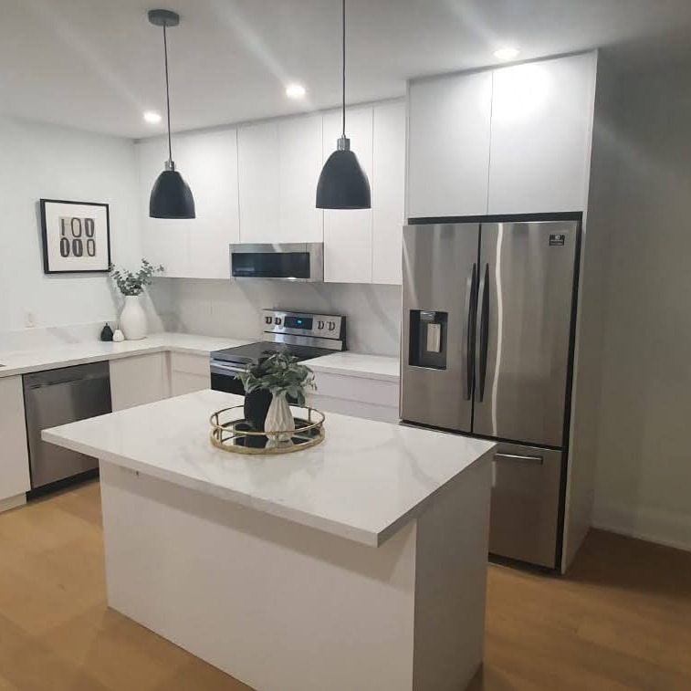 Nowoczesna kuchnia z białymi szafkami, wyspą i dwoma czarnymi lampami wiszącymi nad nią. Oświetlenie punktowe w suficie. Minimalistyczny design.