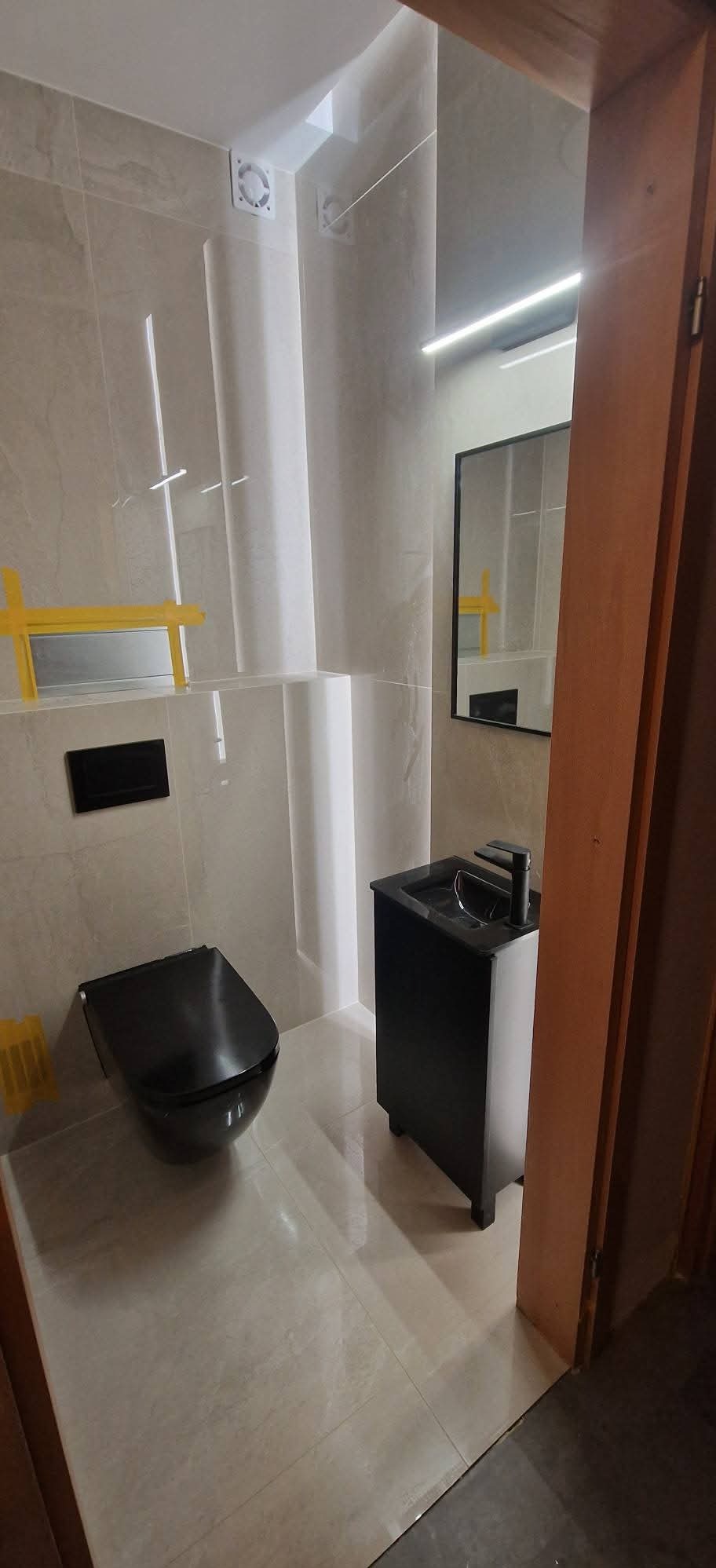 Nowoczesna łazienka z beżowymi płytkami, czarną armaturą i podświetleniem LED. Uwagę zwraca wisząca toaleta i minimalistyczna umywalka z szafką.