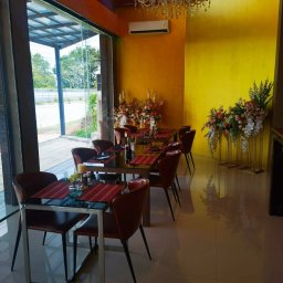 AGRemUS - Eleganckie wnętrze restauracji z żółtą ścianą, stolikami nakrytymi do posiłku i dekoracjami kwiatowymi. Widoczne krzesła z brązowej skóry i szklane elementy.