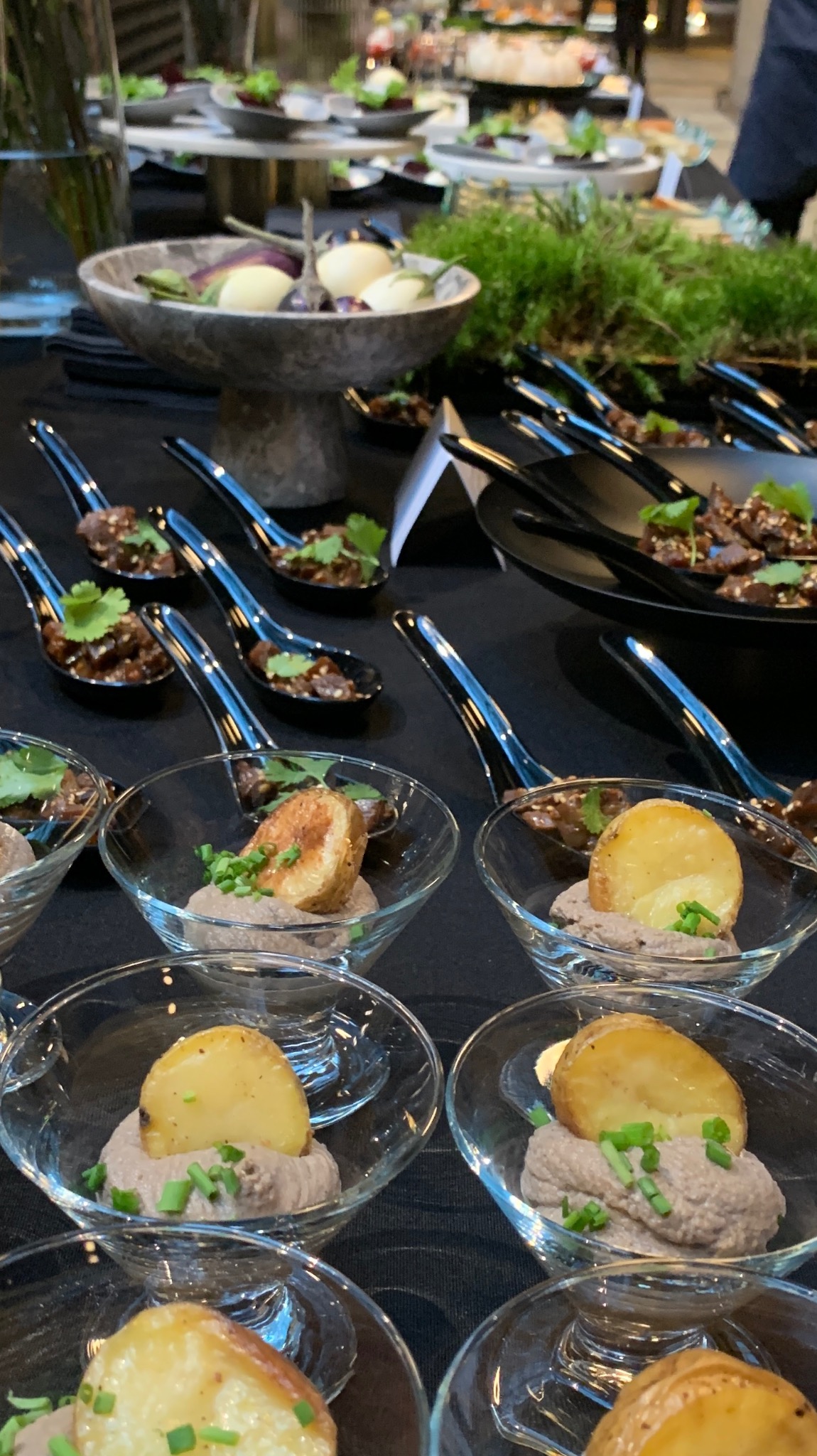 Elegancki catering: ziemniaki na musie w szklanych miseczkach i mięso w czarnych łyżkach na stole z dekoracjami roślinnymi. Wyrafinowane przekąski na przyjęciu.