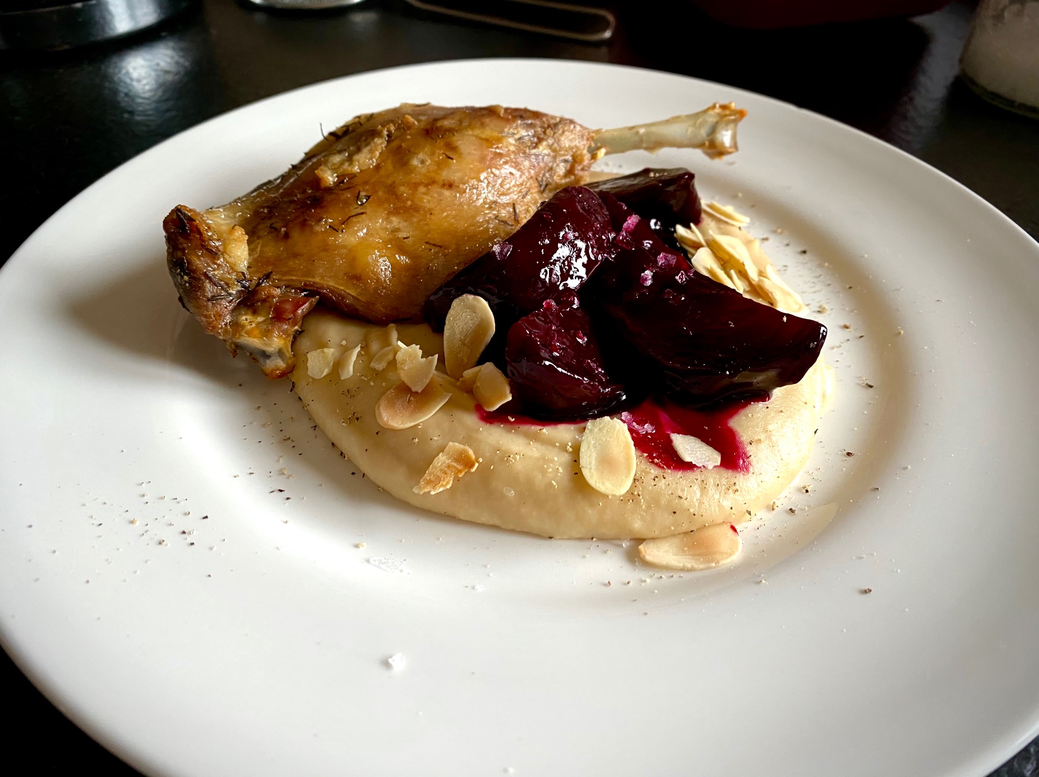 Elegancko podane danie: pieczona noga z kaczki z buraczkami i puree, posypane płatkami migdałów na białym talerzu. Fine dining.