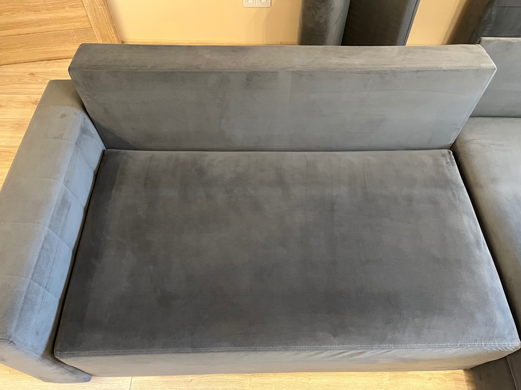 Szary narożnik z welurową tapicerką, widok z góry na siedzisko i oparcie. Minimalistyczny design, jasna drewniana podłoga w tle.