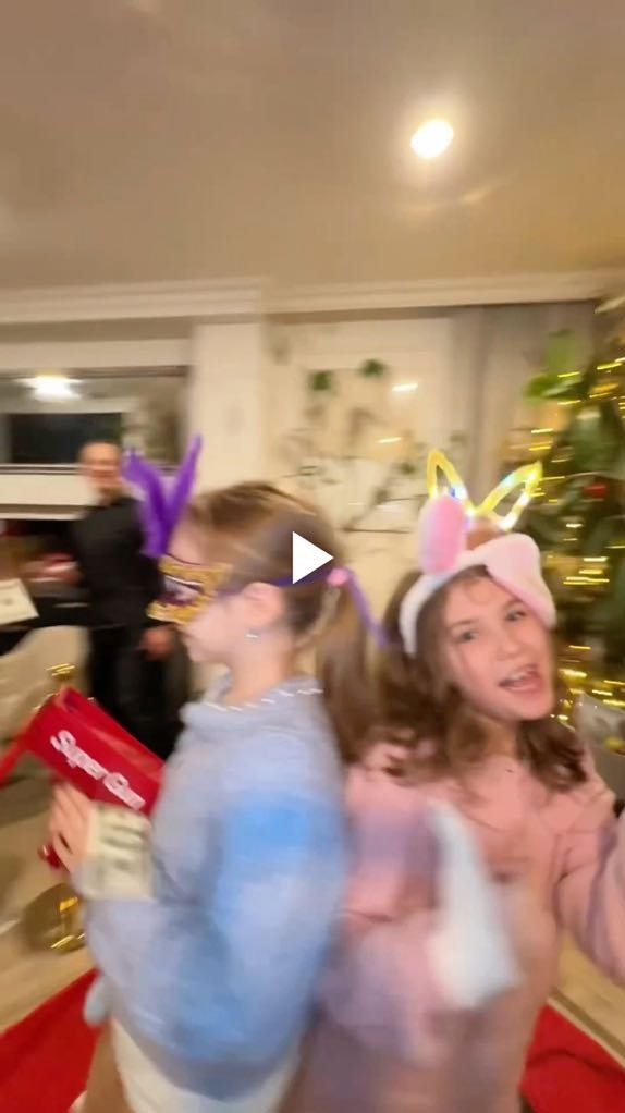 Dwie dziewczynki w karnawałowych przebraniach, jedna z pistoletem na pieniądze, w tle mężczyzna i choinka. Rozmazane ujęcie z imprezy.