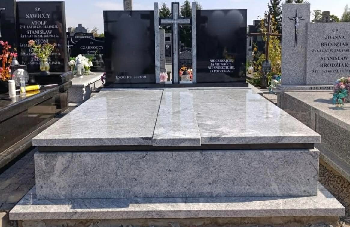 Elegancki, podwójny nagrobek z czarnego i szarego granitu z krzyżem, otoczony innymi pomnikami na cmentarzu w Siedlcach. Widoczne inskrypcje i kwiaty.