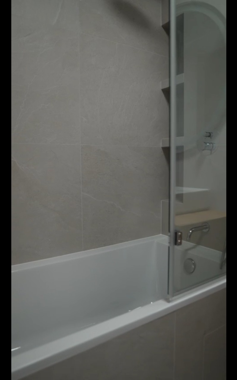 Wykończona łazienka z wanną, szklanym parawanem nawannowym i szarymi płytkami imitującymi kamień na ścianie. Minimalistyczny design.