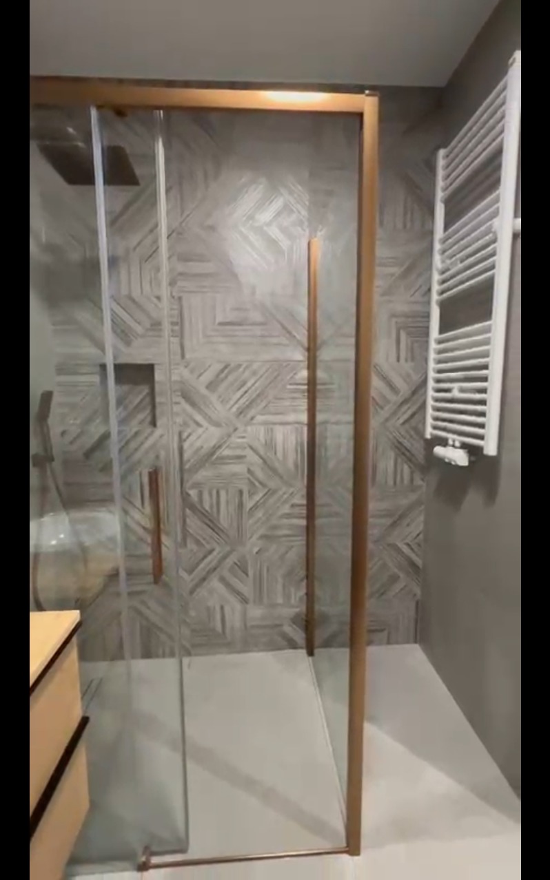 Nowoczesna kabina prysznicowa z geometrycznymi płytkami w odcieniach szarości i beżu, z grzejnikiem drabinkowym na ścianie. Minimalistyczny design.