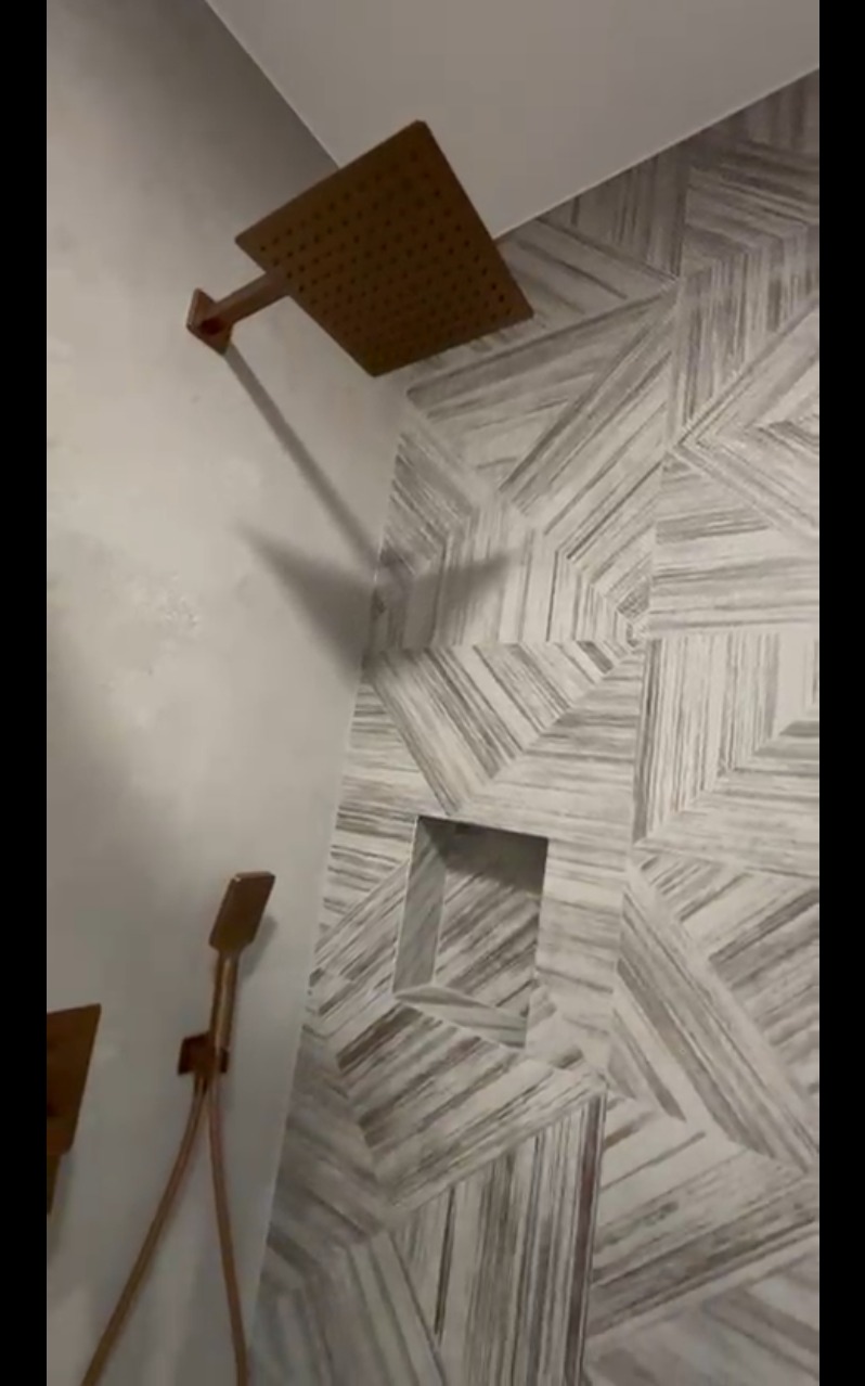 Wykończona łazienka z mozaikową ścianą, wnęką i miedzianą armaturą prysznicową. Nowoczesny design z dbałością o detale.