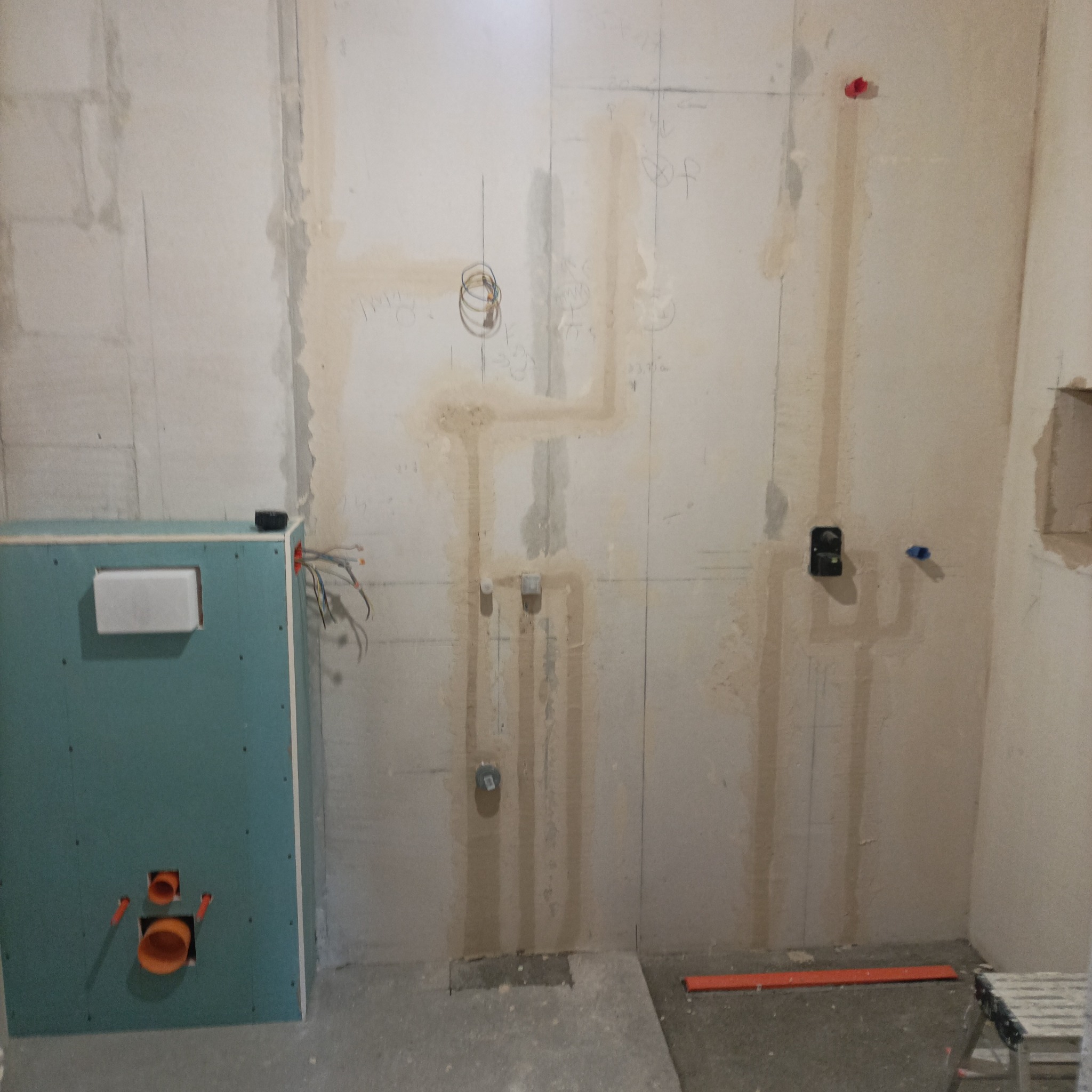 Niedokończona łazienka w trakcie prac: widoczne instalacje wodne, elektryczne i stelaż podtynkowy z płyty GK. Ściany przygotowane do dalszych prac wykończeniowych.