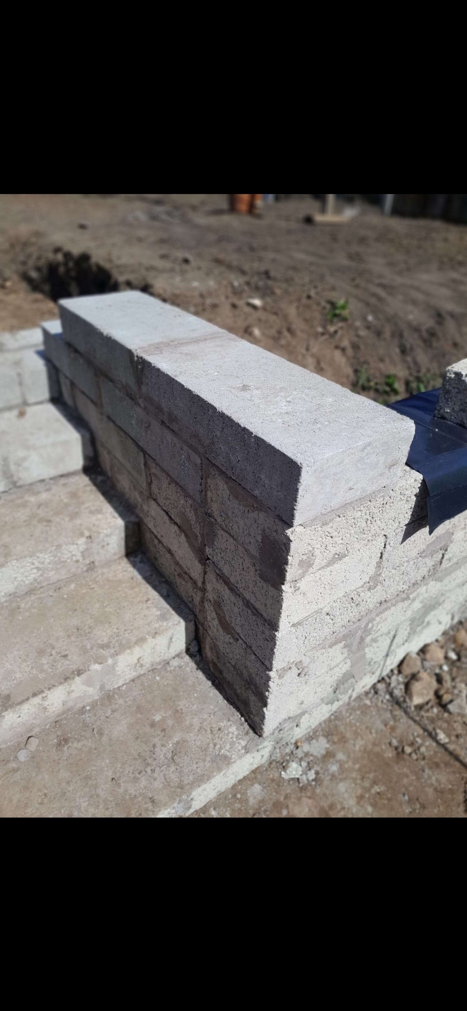 Fragment murowanej konstrukcji z szarego betonu komórkowego na zewnątrz, widoczna warstwa hydroizolacji. W tle ziemia i roślinność.