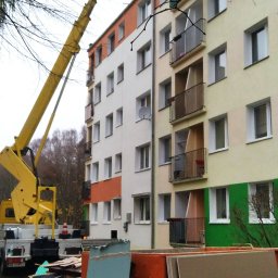 Dar-bud usługi ogólno budowlane - Żółty podnośnik koszowy przy bloku, płyty gipsowe i gruz na ziemi. Remont elewacji budynku wielorodzinnego w trakcie prac.