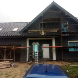 Dar-bud usługi ogólno budowlane - Dom jednorodzinny w trakcie ocieplania, widoczne rusztowania i materiały izolacyjne. Okna zabezpieczone folią, przygotowania do elewacji.